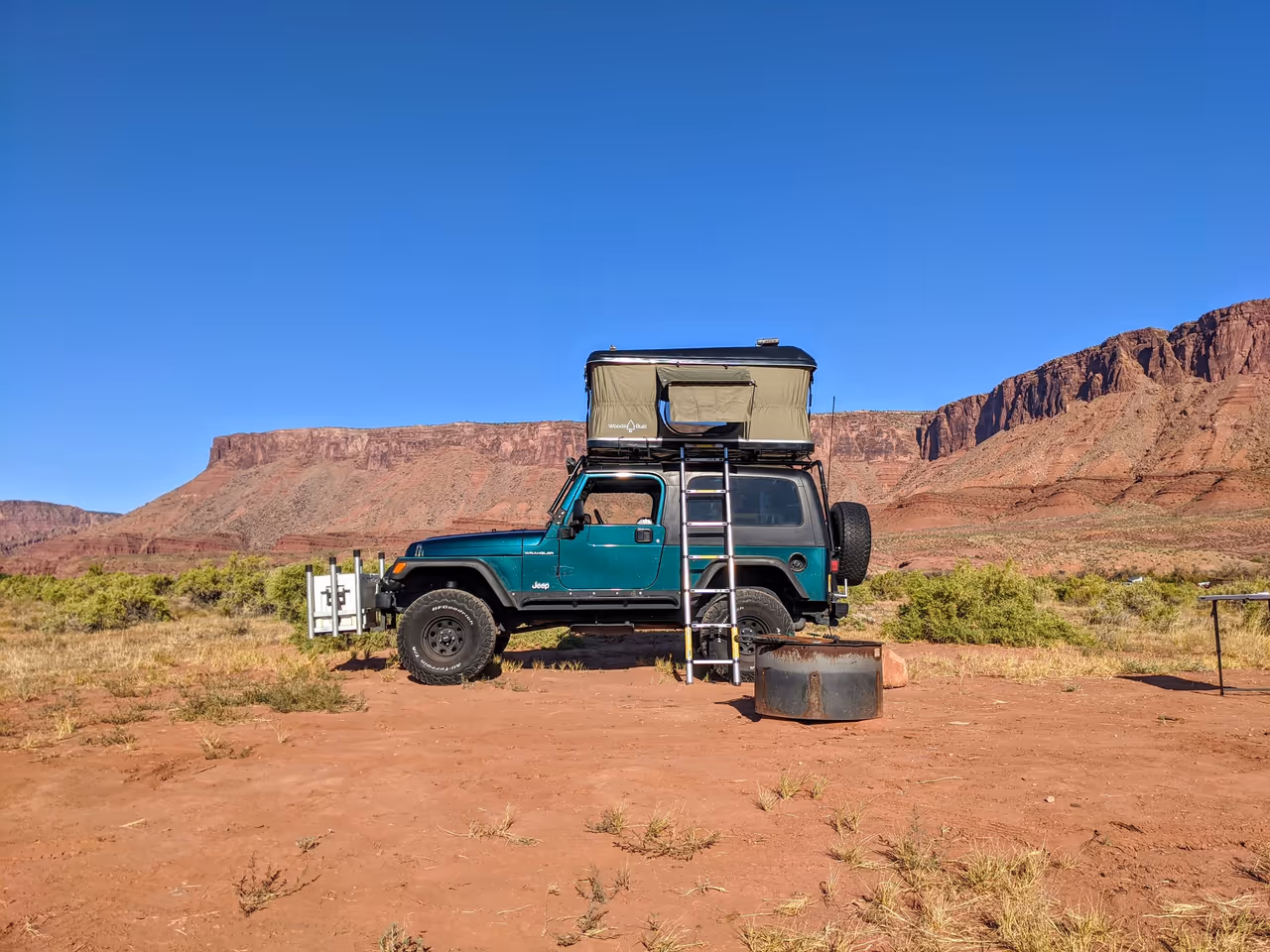 A Jeep with a rooftop tent below red rock cliffs